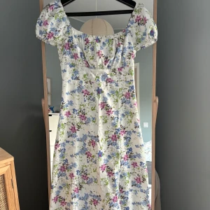 Blommig klänning med puffärmar - Superfin blommig klänning i vitt med blommönster i blått, rosa och grönt 🌸Klänningen har puffärmar och en smockad rygg, slutar vid vaderna på mig som är 167. Perfekt för vår och sommar☀️Använd 1 gång!