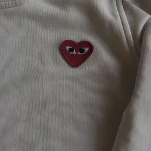Vit tröja från Comme des Garçons(play) - Säljer en stilren vit tröja från Comme des Garçons med ett ikoniskt rött hjärta med ögon på bröstet. Tröjan har långa ärmar och en rund halsringning. Perfekt för en minimalistisk look.