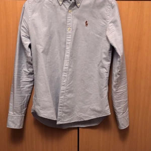 Ljusblå skjorta från Ralph Lauren - Säljer denna snygg ljusblåa skjorta från Ralph Lauren i 100% bomull på grund av att den är för liten. Skjortan har en klassisk krage och broderad logotyp på bröstet. Perfekt för en stilren look och självfallet äkta. 