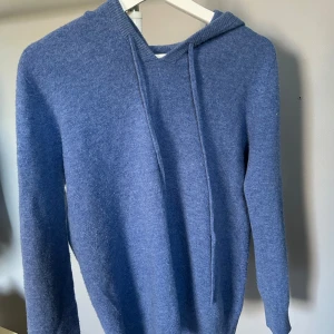 Blå Kashmir hoodie - Säljer en mysig blå kashmir hoodie med långa ärmar och en praktisk huva. Perfekt för kyliga dagar och ger en avslappnad stil. Passar både till jeans och mjukisbyxor.