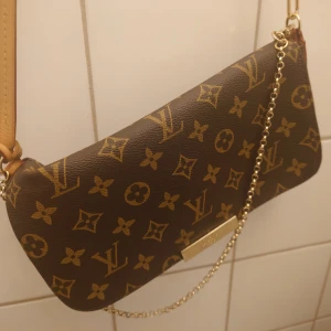  Vintage axelväska Louis Vuitton MM favorite - Säljer en elegant brun axelväska från Louis Vuitton modell MM favorite . Inredningen är i vinröd canvas ( blev lite ljusare på bilden tyvärr).                Väskan är i skick B = bra använt skick, lite små ytliga repor på  emblem samt man ser spår av användning inuti väskan.           I övrigt otroligt fin väska och allt läder i perfekt skick. Mått ; 23.5 x 15 cm datum kod TD 0175 tillv i Italien 2015 Vecka 7. Har inte kvar kvar org kvitto,förpackning ägd av familjen sedan 2019.