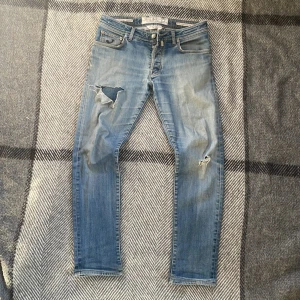 Blå Jacob Cohen jeans med slitningar - Säljer ett par riktigt snygga Jacob Cohen jeans med snygga slitningar, slim passform. Litet hål i skrevet annars bra skick. Pris är diskuterbart, skriv om du har några frågor!