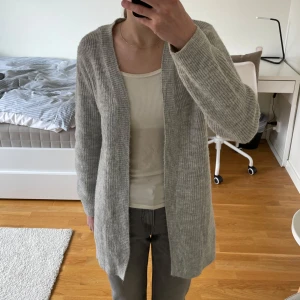 Grå kofta från KappAhl - Mysig grå kofta från KappAhl i en mjuk stickad design. Perfekt för kyliga dagar med sin långa passform och bekväma ärmar. En stilren och enkel baströja för alla tillfällen.