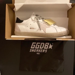 Vita sneakers från Golden Goose - Snygga vita sneakers från Golden Goose med en ikonisk stjärndetalj i grå mocka på sidan. Skorna har grå snörning och en smutsig look på sulan för en vintage känsla. Perfekta för en avslappnad stil.