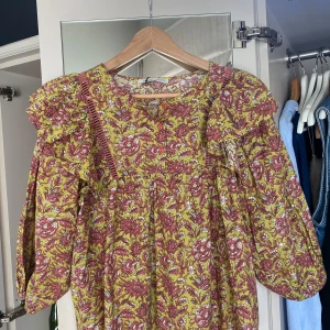 Blommig blus från Pull&Bear - Säljer en färgglad blommig blus från Pull&Bear. Blusen har volangdetaljer vid axlarna. Den är i en härlig kombination av rosa och gul med ett vackert blommönster. Perfekt för att liva upp garderoben!