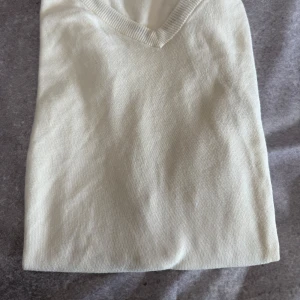 Vit v-ringad väst från Chaps - Säljer en stilren vit v-ringad väst från Chaps. Västen är tillverkad i 100% bomull och har en diskret broderad logga på bröstet. Perfekt för en klassisk och avslappnad look. Passar även XL.