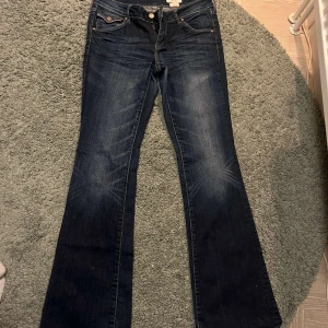 Mörkblå bootcut jeans - Snygga mörkblå bootcut jeans med klassisk femficksdesign och knappgylf. Jeansen har en lätt tvättad look och är perfekta för en avslappnad stil. Passar bra till både sneakers och stövlar. Midjemåttet är 74!