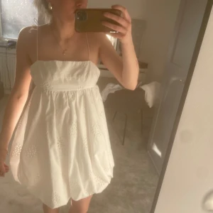Vit klänning med broderade detaljer - Säljer en söt vit klänning med tunna axelband och broderade detaljer. Klänningen har en öppen rygg med snörning och en luftig passform. Perfekt för varma sommardagar!