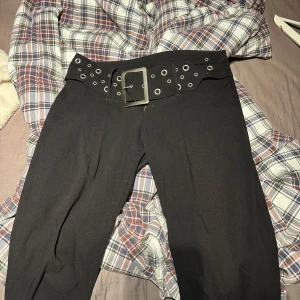 Svarta byxor med bälte - Snygga svarta byxor med ett brett inbyggt bälte och silverfärgade detaljer. Byxorna är lowwaist och vida ben, vilket ger en avslappnad stil. Perfekta för en trendig look. Lite smuts längst ner i bak på benen men de går bort i tvätt
