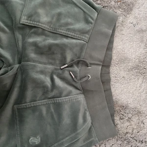 Gröna mjukisbyxor Juicy Couture S - Mysiga gröna mjukisbyxor från Juicy Couture i velour med bred resår och snörning i midjan. Byxorna har raka ben, stora fickor fram och diskret Juicy Couture-logga på fickan. Perfekta för chill dagar eller när du vill vara extra comfy.