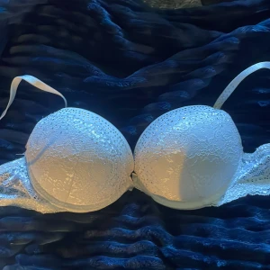 Vit spetsig bh med strassdetaljer - Supersnygg vit bh med spets och glittrande strassdetaljer över kuporna. Justerbara band och vacker spets längs kanterna. Perfekt för dig som vill ha något extra under outfiten.