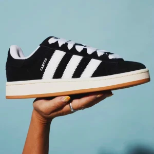 Adidas Campus svarta sneakers - Adidas Campus sneakers i svart mocka med vita klassiska ränder på sidorna och vit text. Skorna har tjocka vita snören, rund tå och en beige gummisula. Perfekt för dig som gillar retrostil och vill ha en clean look med street vibe.