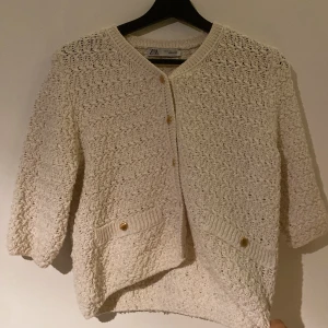 Glittrig beige kofta från Zara - Superfin beige kofta från Zara med glittriga inslag i materialet och snygga guldknappar framtill. Koftan har trekvartsärm och två fickor med dekorativa knappar. Perfekt att slänga över en topp för en chill men ändå stylish look.