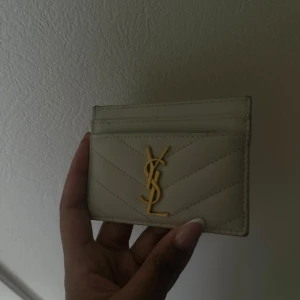 Vit YSL kortfodral i skinn - ÄKTA VARA!! Supersnyggt vitt kortfodral från YSL i skinn med guldigt logomärke framtill. Stilren design med diskreta sömmar i chevronmönster och flera kortfack. Perfekt accessoar för dig som vill ha något lyxigt och minimalistiskt i fickan.