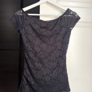 Svart spettopp offshoulder - Säljer en svart topp i spets med offshoulder-modell. Toppen har korta ärmar och ett blommigt spetsmönster. 