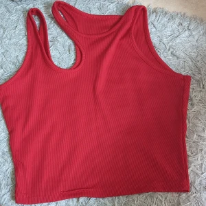 Röd ribbad croppad topp - Snygg röd croppad topp med ribbad struktur och breda axelband. Perfekt för varma dagar eller att styla lager på lager. Enkel och stilren design som passar till jeans eller kjol. (Inte lika röd som på bild)