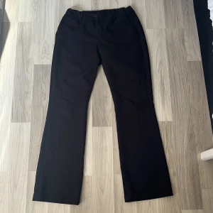 Svarta kostymbyxor från BikBok (Vera) - Klassiska svarta kostymbyxor från BikBok i rak modell med lätt utsvängda ben. Byxorna har hällor för bälte, fickor fram och bak samt stängs med dragkedja och knapp. Perfekta för en clean och stilren look. Byxorna har en låg midja och är även lite insydda i midjan. Pris kan diskuteras.