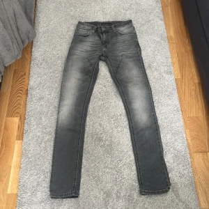 Grå skinny jeans från Nudie Jeans - Snygga grå jeans från Nudie Jeans i modellen skinny med klassisk femficksdesign och coola slitningar. Jeansen har en smal passform och är tillverkade i mjukt denimtyg som sitter skönt hela dagen. Perfekt för dig som gillar en modern och stilren look.