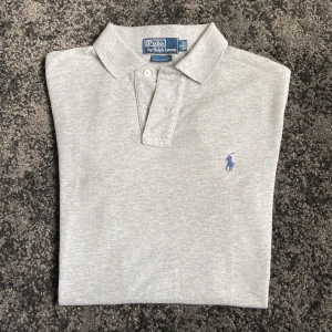 Grå Ralph lauren piké - Säljer denna Ralph lauren piké som är i perfekt skick utan några defekter. Custom fit-modell i mjuk bomull. Hojta till om du har någon fråga!