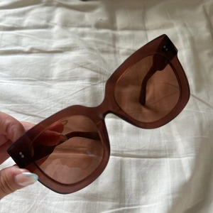 Chimi solglasögon  - Stilrena oversized solglasögon i brun transparent plast med fyrkantig form. Bågarna är breda och ger en cool retrovibe. Perfekta för att lyfta din look med en touch av vintagekänsla. Snygga detaljer med små silvriga prickar vid bågens hörn.