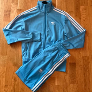 Adidas tracksuit - Snygg blå Adidas tracksuit med klassiska vita ränder längs ärmarna och broderad logga på bröstet. Storlek XS. Jackan har hög krage, dragkedja framtill och ribbade muddar. Använd ett fåtal gånger och är därför i bra skick. Perfekt för en sportig och avslappnad stil. Pris kan diskuteras