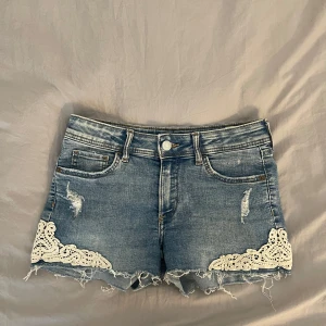 Blå jeansshorts med spetsdetaljer 🤍💙 - Snygga blå jeansshorts med råa kanter och slitningar, dekorerade med vita spetsdetaljer. Dom sitter även lite lågmidjat, det går även att vika ner dom om man önskar att ha ännu lägre midja 🫶🏼