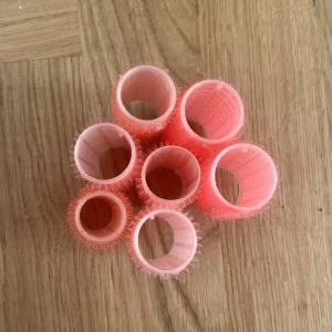 Rosa och röda papiljotter  - Säljer ett set med sju papiljotter i olika nyanser av rosa och rött. Spolarna är gjorda i plast med kardborre-yta som gör det enkelt att rulla upp håret och få volym. Perfekt för att fixa snygga lockar eller vågor hemma. Ganska små så man får ett tydligt resultat!