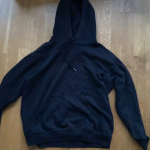 Svart hoodie från H&M Basics - En klassisk svart hoodie från H&M Basics i storlek S. Tröjan har huva med snörning, magficka och ribbade muddar vid ärmslut och nederkant. Materialet är mjukt och skönt. Du står för frakten, vid mer info skriv 