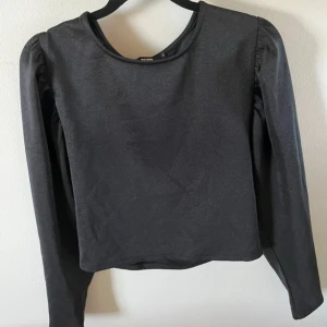 Svart långärmad topp från Bik Bok - En stilren svart långärmad topp från Bik Bok med rund halsringning och lätt puffade axlar. Materialet känns mjukt och stretchigt, vilket gör den bekväm att bära hela dagen.