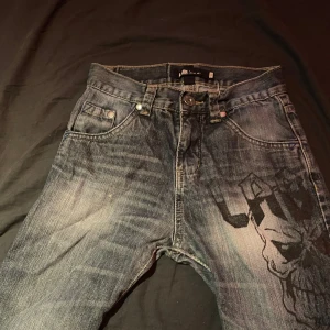Jeansshorts med tryck från LTB Industries - Snygga jeansshorts från LTB Industries i mörkblå denim med coolt svart tryck på ena benet. Shortsen har klassiska fem fickor, slitna kanter och detaljerade bakfickor med guldiga sömmar och metalldetaljer. Perfekta för en avslappnad streetstil.