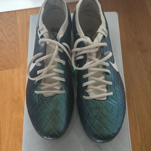 NIKE TIEMPO LEGEND 10 ELITE FG EMERALD - TURKOS/VIT LIMITED EDITION - LIMITED EDTION! Snygga fotbollsskor från Nike med grön metallicfärgad ovandel och vita detaljer. Skorna har ett rutmönster på ovandelen, vita snören och vit Nike-logga på sidan. Perfekt för dig som vill sticka ut på planen! Skorna är knappt använda.