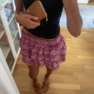 Rosa mönstrad kortkjol Meet x Tiger - Supersöt kortkjol från Meet x Tiger i rosa med paisley-inspirerat mönster. Kjolen har smockad midja och volangkant som ger en feminin vibe. Perfekt för varma dagar och enkel att styla med en crop top eller linne.