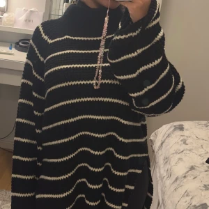 Svartvit randig polotröja stickad - Säljer en oversized stickad polotröja med svart botten och vita ränder. Tröjan har lång ärm och hög krage, perfekt för att hålla dig varm och snygg. Den har en loose passform och är supermysig att bära under kyliga dagar.