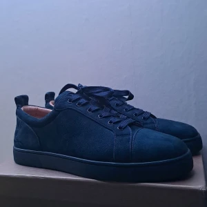 Louboutin sneakers - Snygga mörkblå sneakers i mocka från Christian Louboutin med klassisk röd sula och rund tå. Skorna har svarta snören och diskreta detaljer, perfekt för dig som gillar stilrena och exklusiva sneakers med lyxig känsla.