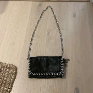 Svart axelväska med kedja  - Säljer en svart axelväska i skinn med grov silverfärgad kedja som axelrem. Väskan har snygga kedjedetaljer runt kanterna och stängs med magnetknappar. Perfekt storlek för det viktigaste och ger en cool vibe till outfiten. Säljer pga av nästan ingen användning. Den har rostat lite på kedjan men annars har den inte rostat någon annanstans. Kommer tyvärr inte ihåg var den är ifrån men tror att den är från Scorett! Skriv om ni vill diskutera pris eller om ni undrar något!💗