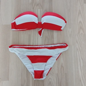 Rödvit randig bikini bandeau - Snygg bikini med breda röda och vita ränder. Överdelen är bandeau-modell med knyt framtill och underdelen är klassisk trosa. Perfekt för stranden eller poolen. Fräsch och färgstark look som sticker ut i sommar.