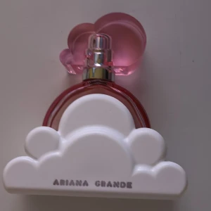 Ariana Grande Cloud Pink Parfym - Superfin parfym från Ariana Grande i en rosa rund flaska med ett stort vitt moln som dekor. Locket är format som ett rosa moln och flaskan har silvriga detaljer. Perfekt för dig som gillar söta och fräscha dofter och vill ha en snygg parfym på hyllan. Storlek 30 ml men lite mindre än hälften kvar 