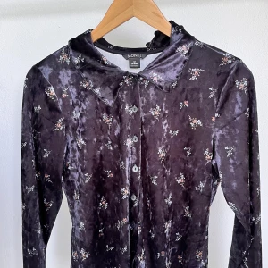 Mörklila blommig sammetskjorta Monki - Supersöt långärmad skjorta från Monki i mörklila sammet med små blommiga mönster. Skjortan har klassisk krage, knäppning framtill och en mjuk, glansig finish som ger en lyxig känsla. Perfekt för dig som gillar unika och trendiga plagg!