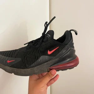 Nike Air 270 svarta sneakers med röd detalj - Nike Air 270 sneakers i svart mesh med röda swoosh-detaljer och stor synlig luftbubbla i rött på hälen. Skorna har snörning, rund tå och en sportig vibe. Perfekta för dig som gillar streetstyle och vill ha bekväma och snygga sneakers.