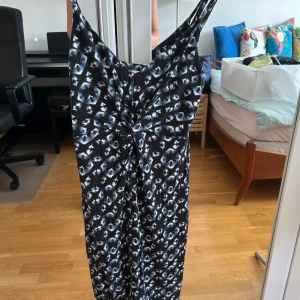 Svart och blå mönstrad långklänning H&M - Säljer en långklänning från H&M i storlek S med svart och blått geometriskt mönster. Klänningen har smala axelband och en snygg twistad detalj framtill. Materialet är mjukt och stretchigt, perfekt för dig som gillar coola prints och bekväm passform.