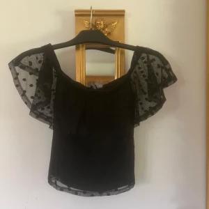 Svart prickig offshoulder topp - Snygg svart offshoulder topp i storlek xs med transparenta volangärmar med svarta prickar. Änvänd men i bra skicka