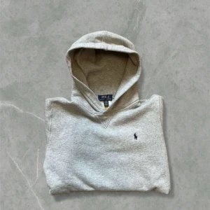 Grå hoodie från Polo Ralph Lauren - Snygg grå hoodie från Polo Ralph Lauren med klassisk huva. Tröjan har ett litet broderat Polo-logo på bröstet och är tillverkad i mjuk bomullsmix. Det är mycket bra skick och det är barn storlek (14-16) vilket motsvarar xs i herrstorlek.