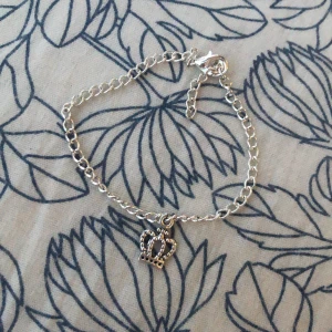 Handgjort silverfärgat armband med kronberlock. - Snyggt armband i silverfärg med en kedja och en detaljrik kronberlock som hänger i mitten. Länken är justerbar med ett litet lås och passar perfekt om du gillar stilrena accessoarer med en touch av royalty. Kronan har små prickdetaljer som gör den extra cool.