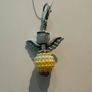 Halsband med pärlängel i silver och gult - Unikt halsband med en ängel som hänge, tillverkad av silverfärgad metall och pärlor i gult och vitt. Vingarna är detaljerade och kroppen består av glansiga pärlor. Perfekt för dig som gillar personliga smycken med lite extra charm.