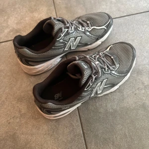 Grå New Balance sneakers mesh - Snygga grå sneakers från New Balance med klassisk siluett och ventilerande mesh-ovandel. Skorna har vita och svarta detaljer, snörning och en bekväm, tjock sula. Perfekta för dig som gillar sportig stil och vill ha något som funkar till streetwear.