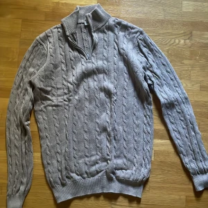 Beige stickad tröja med half zip - Säljer en beige stickad tröja från John Henric i storlek M. Tröjan har kabelstickat mönster, ribbad krage och en snygg half zip-dragkedja. Perfekt för dig som gillar klassisk stil med en modern twist. Långärmad och riktigt skön att bära under kyliga dagar.