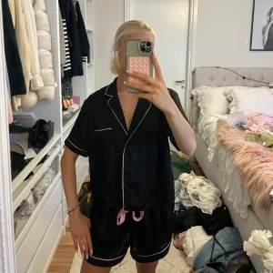 Svarta pyjamasshorts från Primark - Svart pyjamasshortsset från Primark köpt i London med ljusrosa kantband och snörning i midjan. Mjukt och lätt material som känns skönt mot huden. Perfekt för chill dagar hemma eller mysiga kvällar. Klassisk loose fit och snygg kontrast med de rosa detaljerna.