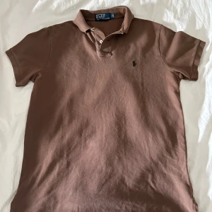 Brun pikétröja Ralph Lauren storlek M - Riktig bra skick Säljer en brun pikétröja från Polo Ralph Lauren i modellen Custom Fit. Klassisk krage, korta ärmar och broderad logga på bröstet. Perfekt för en clean och stilren look. Materialet är mjuk bomull som andas. Jag skickar snabbt