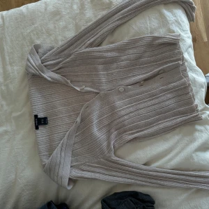 Beige ribbad kofta från Lindex - Säljer en beige ribbad kofta från Lindex i storlek XS. Koftan har långa ärmar, knappar framtill och är gjord i ett mjukt stickat material. Perfekt att slänga över en t-shirt eller linne för en chill look. Snyggt ribbad struktur och neutral färg som passar till allt.