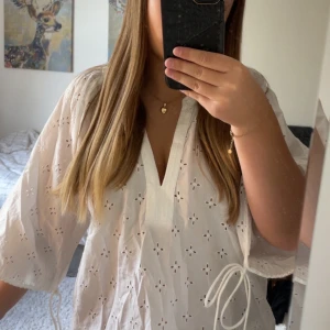 Vit blus med broderade detaljer Lindex - Säljer en vit blus från Lindex i storlek S. Blusen har broderade hålmönster i form av små blommor, v-ringad hals och knytband vid sidorna. Luftig och lätt i bomull, perfekt för varma dagar. Ärmarna är halvlånga och ger en chill vibe. Endast testad